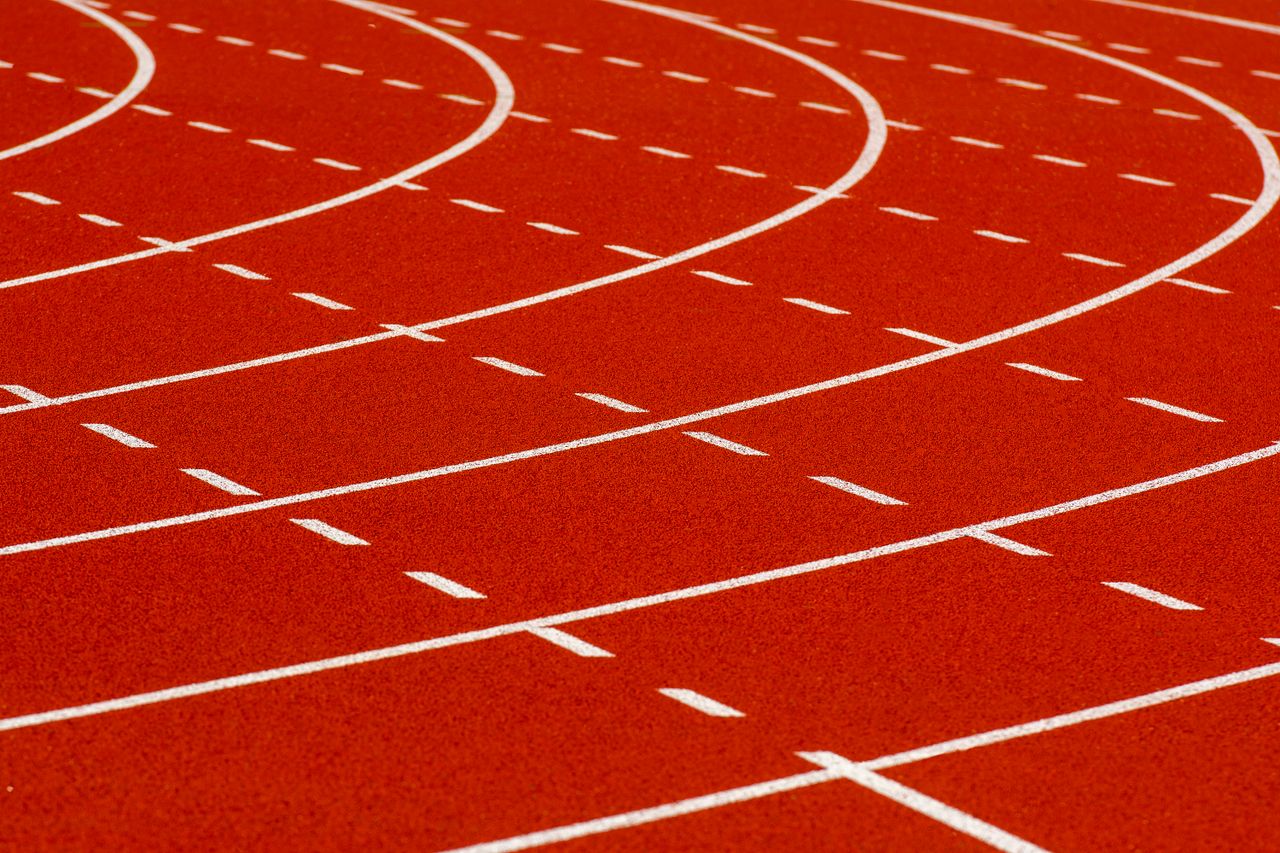 Close-up view of a curved red running track with dashed white lines for athletic sports.